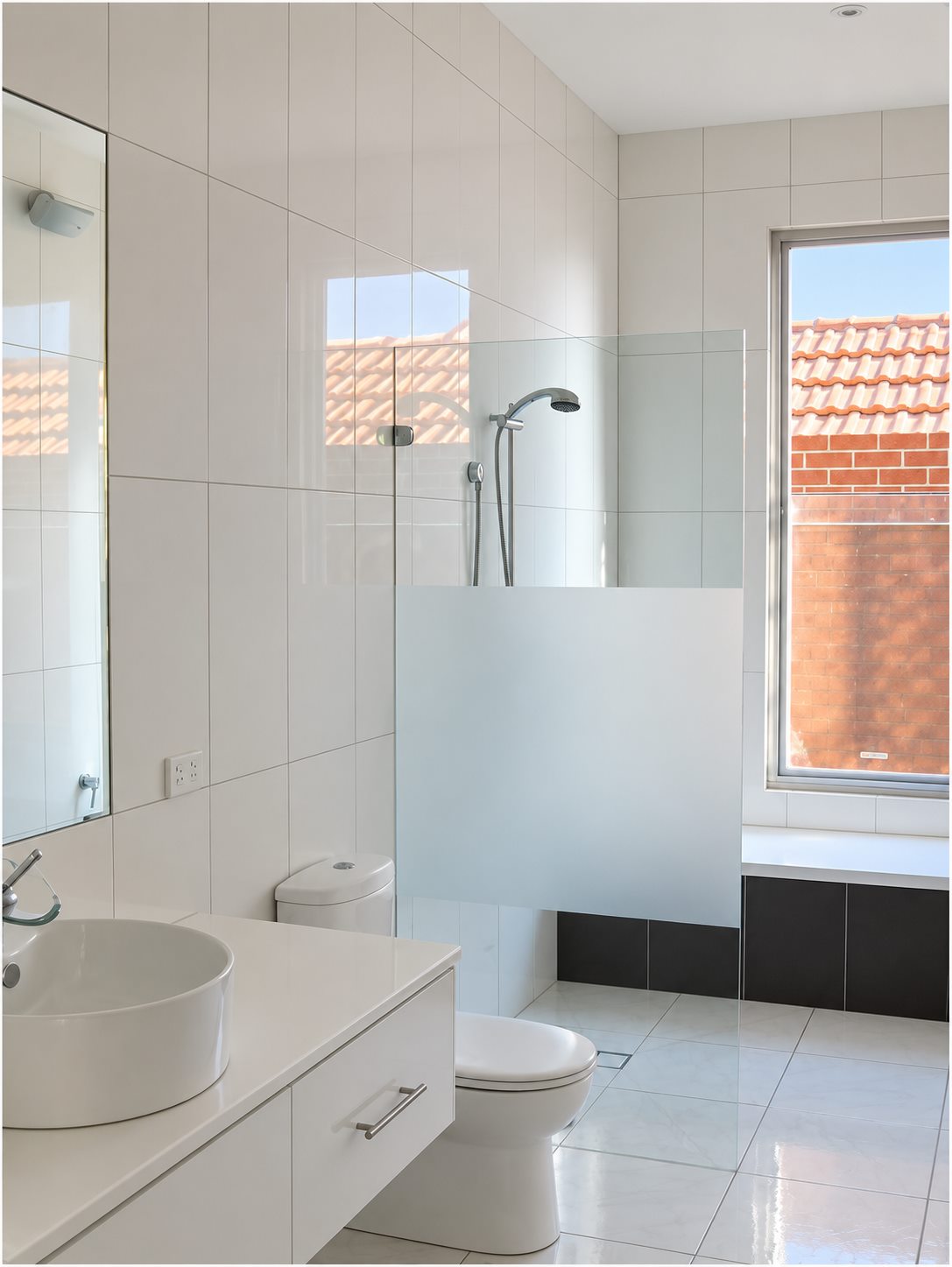 Bathroom: white tile, a frameless screen and a window onto the neighbouring roofs