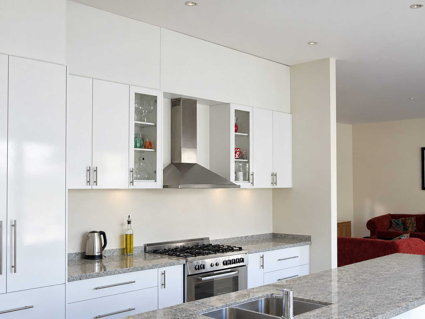 The kitchen, white joinery and a stone bench under a stainless hood