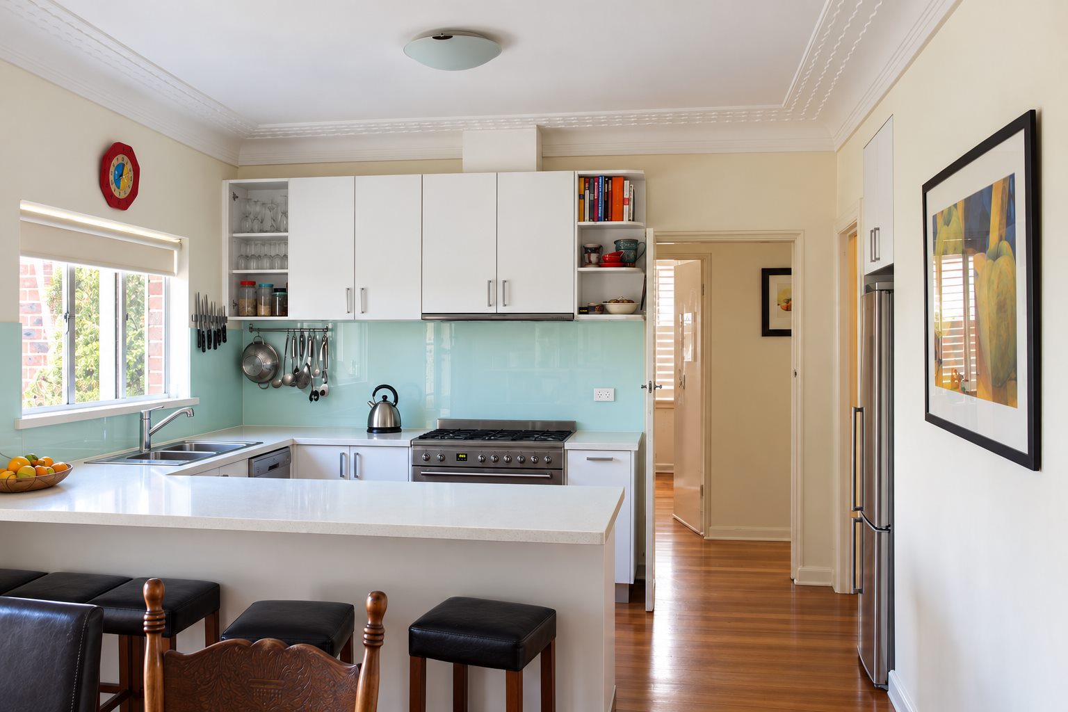 The existing kitchen, white cabinetry and a mint glass splashback behind a peninsula bench