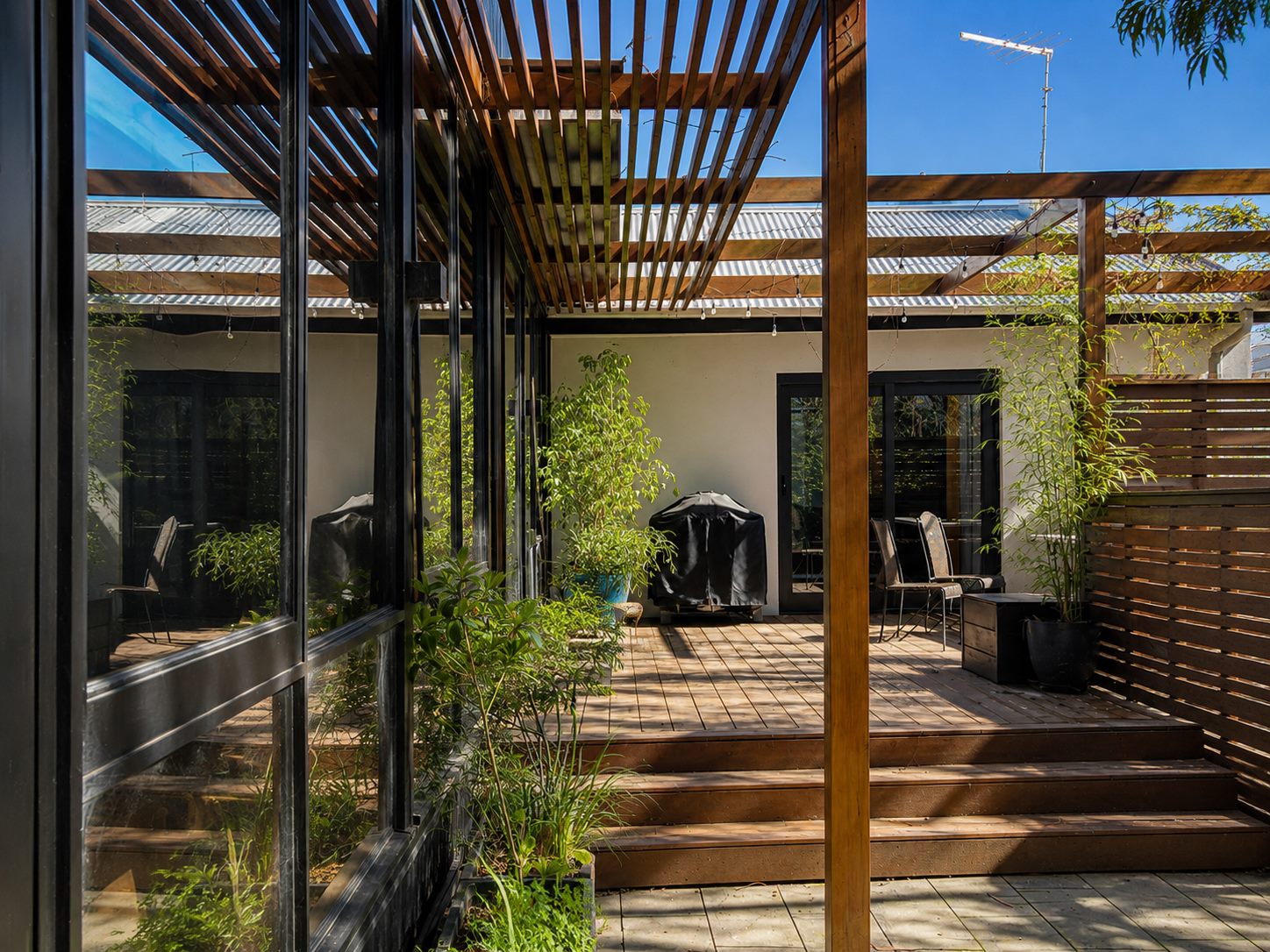 The courtyard under the pergola, enclosed by black-framed glazing